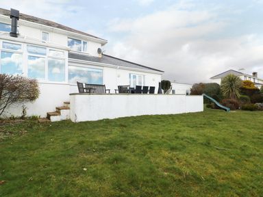 A backyard with a raised patio with wooden chairs and a table and a slide next to a white house at The Beach House Criccieth