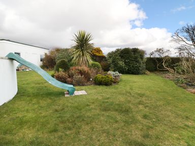 A garden area with a green slide attached to a white building and various bushes at The Beach House Criccieth