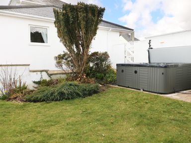 A backyard with a grassy lawn shrubs and a hot tub beside a white house at The Beach House Criccieth
