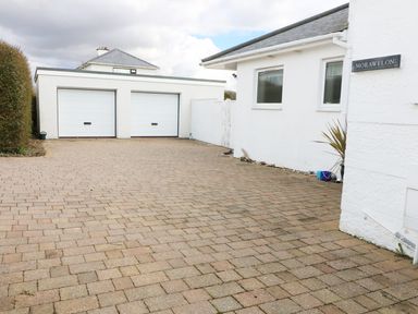 A driveway with a double garage and a white house with two windows and a plant at The Beach House Criccieth