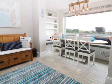 A dining area with a wooden bench, white chairs around a wooden table and a large window at The Beach House Criccieth in Criccieth