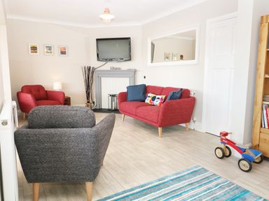 A living room with red and gray armchairs a red sofa a wall-mounted TV and a small wooden bike at The Beach House Criccieth