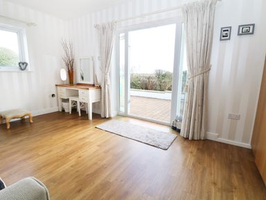 A room with wooden floor a white dressing table with a chair a window and sliding glass doors with curtains pointing to a patio at The Beach House Criccieth