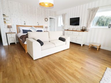 A bedroom with a wooden bed white sofa television and wooden floor at The Beach House Criccieth