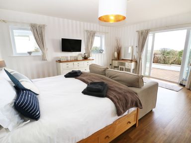 A bedroom with a bed sofa TV dresser vanity and sliding glass door at The Beach House Criccieth