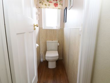 A small bathroom with a toilet wooden floor and a window with floral blind at The Beach House Criccieth