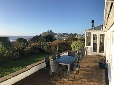 An outdoor patio with a dining table and chairs overlooking a garden and distant castle at The Beach House Criccieth