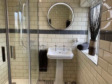 A bathroom with a pedestal sink and a circular mirror above at The Beach House Criccieth