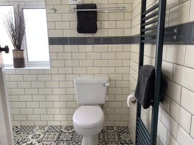 A bathroom with a toilet a patterned tiled floor and black towels on racks at The Beach House Criccieth