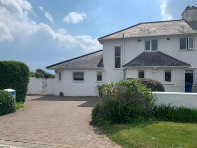 A white two story house with a paved driveway and shrubs in the front garden at The Beach House Criccieth