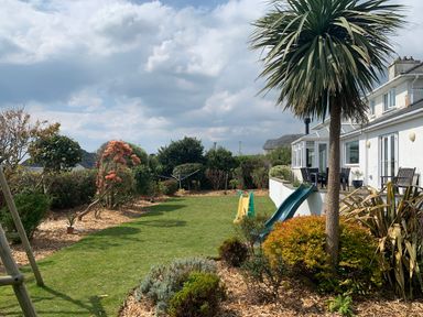 A garden with grass lawn shrubs and a palm tree next to a house with slides and outdoor furniture at The Beach House Criccieth