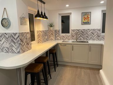 A kitchen with a countertop bar and stools with a sink and cabinets at The Beach House Criccieth Criccieth