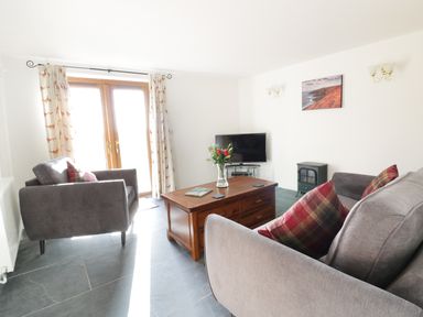 A living room with grey sofas and a wooden coffee table with flowers and a TV at Lower West Curry Cottage in Launceston