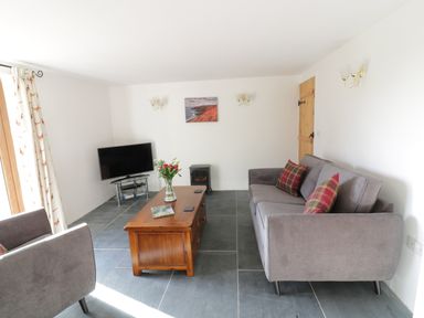 A living room with a gray sofa, wooden coffee table, television, and curtains at Lower West Curry Cottage in Launceston
