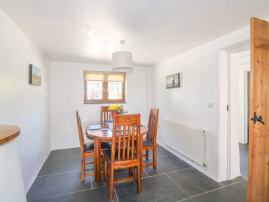 A dining room with wooden table and chairs next to a window and wooden door at Lower West Curry Cottage Launceston
