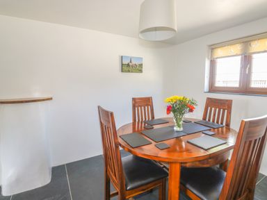 A dining area with a round wooden table and four chairs with placemats and a flower vase on the table at Lower West Curry Cottage in Launceston