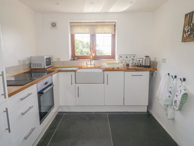 A kitchen with white cabinets wooden countertops microwave oven toaster kettle and window with a chicken themed blind at Lower West Curry Cottage in Launceston