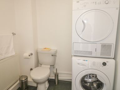 A bathroom with a toilet and stacked washing machine and dryer at Lower West Curry Cottage in Launceston
