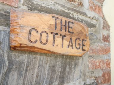 A wooden sign with the words The Cottage on a stone wall at Lower West Curry Cottage in Launceston