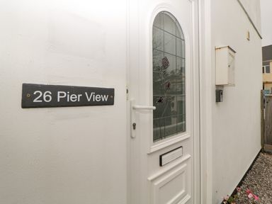A white front door with stained glass and a house number sign on the wall at 26 Pier View in Paighton