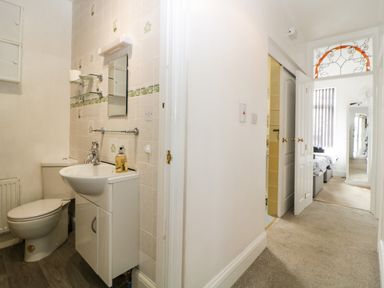 A small bathroom with a toilet and sink next to a hallway leading to a bedroom at Pier View in Paighton