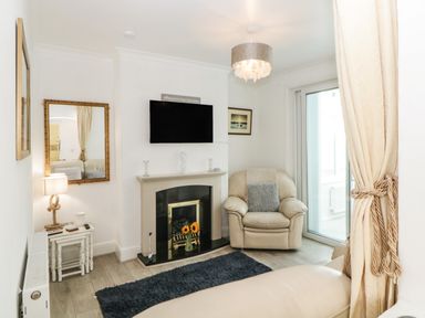 A small living room with a beige armchair a fireplace a wall-mounted TV and a side table with a lamp at Pier View in Paighton
