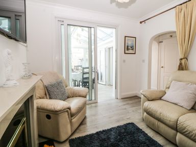A living room with two leather armchairs a sliding glass door leading to a dining area and a wall-mounted television at Pier View in Paighton