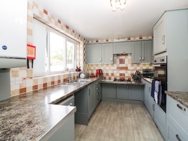 A kitchen with a tiled backsplash gray cabinets double sink stove oven and countertop at Pier View in Paighton