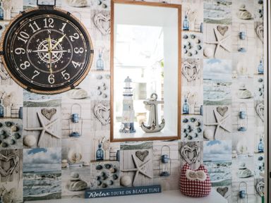 A wall with a large clock a framed mirror decorative lighthouse and anchor and a patterned cushion at Pier View in Paighton