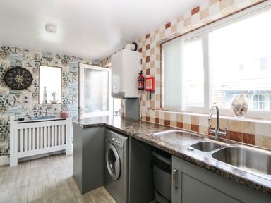 A kitchen with a washing machine under the counter a double sink and a fire extinguisher on the wall at Pier View in Paighton