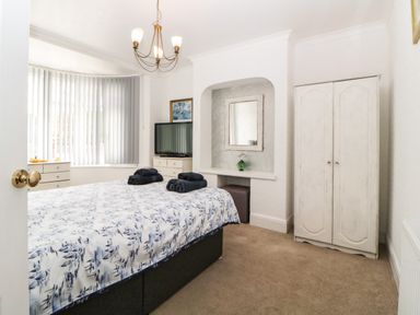 A bedroom with a bed dressed in patterned bedding and towels on top a wardrobe a television on a dresser and a mirror in an alcove at Pier View in Paighton