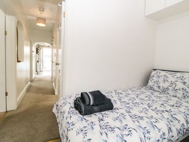A bedroom with a bed and folded towels at the end of the bed and a hallway leading to another room at Pier View in Paighton