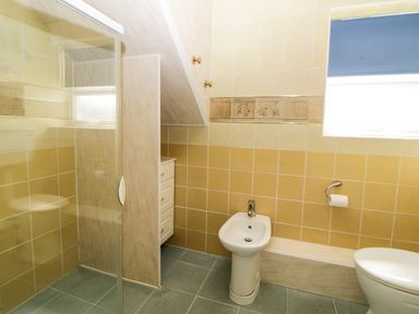 A bathroom with a shower enclosure bidet toilet blue tiled floor and window at Pier View in Paighton