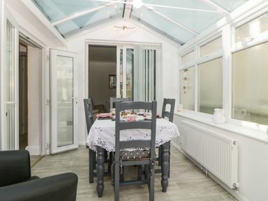 A dining area with a table set for tea and four chairs under a glass roof at Pier View in Paighton
