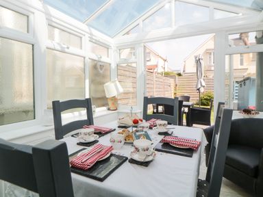 A dining area with a table set for tea and chairs in a conservatory with a view of an outdoor patio at Pier View in Paighton
