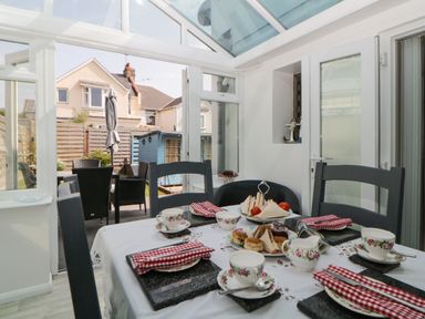 A dining area with a table set for tea including cups, plates, sandwiches, and scones at Pier View in Paighton