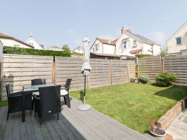 A fenced backyard with a glass table and four black chairs on a wooden deck at Pier View in Paighton