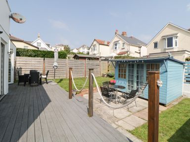 A garden with a wooden deck table and chairs a blue shed and a fenced lawn at Pier View in Paighton