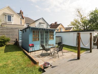 A small blue wooden shed with windows and glass doors in a backyard with a round table and four chairs at Pier View in Paighton
