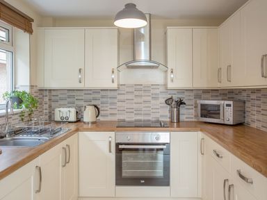 A kitchen with wooden countertops white cabinets a stainless steel oven microwave kettle and toaster at Dartmoor View in Gunnislake