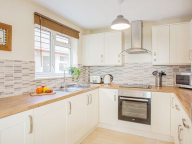 A kitchen with white cabinets wooden countertops a stainless steel oven a microwave a toaster a kettle and vegetables on a cutting board at Dartmoor View in Gunnislake