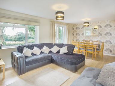 A living room with a black sectional sofa and a wooden dining table with chairs at Dartmoor View in Gunnislake