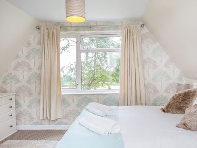 A bedroom with a bed with rolled towels and cushions next to a window with curtains and a chest of drawers at Dartmoor View in Gunnislake