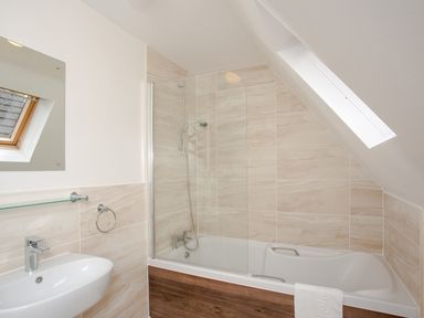 A bathroom with a bathtub shower combination and a sink under a window at Dartmoor View in Gunnislake