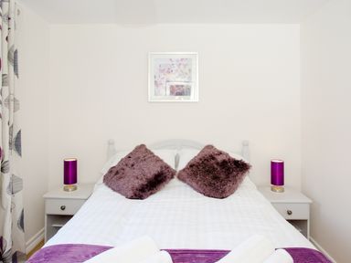 A bedroom with a double bed two purple cushions two bedside tables with lamps and a framed picture on the wall at Dartmoor View in Gunnislake