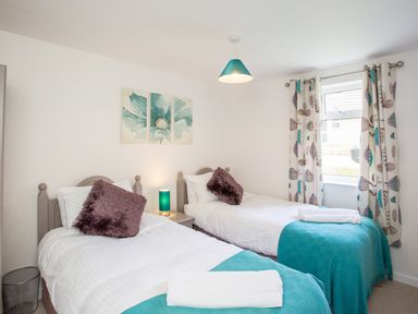 A bedroom with two single beds blue blankets and a window with patterned curtains at Dartmoor View in Gunnislake