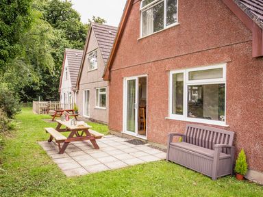A row of houses with outdoor picnic tables on a grassy area at Dartmoor View in Gunnislake