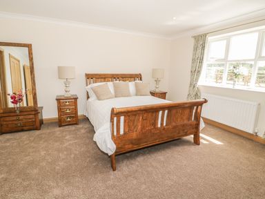 A bedroom with a wooden bed, two bedside tables with lamps, a mirror, and a window at Rede River Cottage in West Woodburn