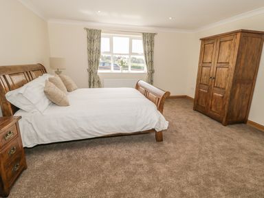 A bedroom with a wooden bed a wooden wardrobe and a window with patterned curtains at Rede River Cottage in West Woodburn