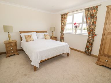 A bedroom with a double bed two bedside tables with lamps a window with floral curtains and a wooden wardrobe at Rede River Cottage in West Woodburn